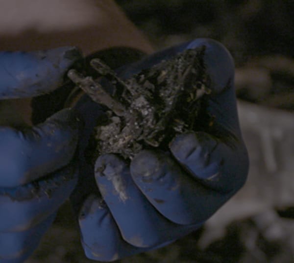 A hand holding a charred mass of electronics.