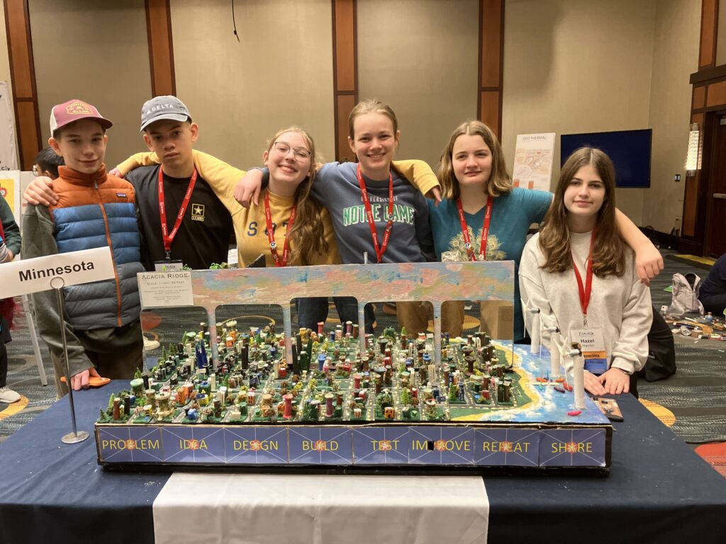 Group of students standing around city model and smiling for photo.
