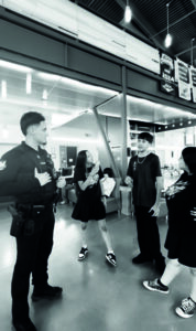 A black and white photo shows three students talking to each other about battery disposal