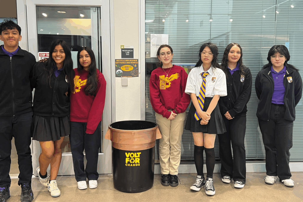 a group of students stands around their battery recycling project, labeled 