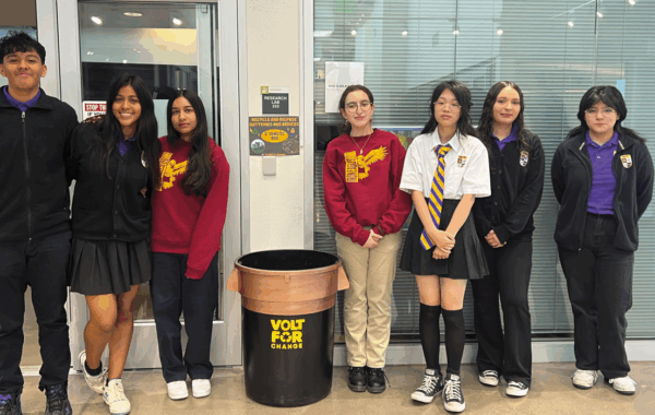 a group of students stands around their battery recycling project, labeled 