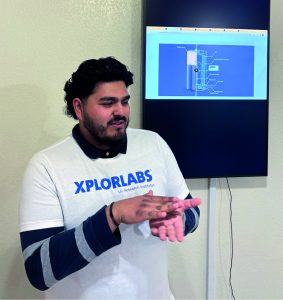 Luis wears an Xplorlabs tshirt and is standing in front of a screen with an Xplorlabs resource shown on the screen