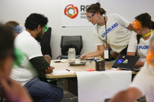a group of Xplorlabs Educator Fellows sitting at a table watching a candle being lit as part of an experiment