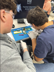 students leaning over their desk, working on an Xplorlabs related project on a blue sheet of construction paper