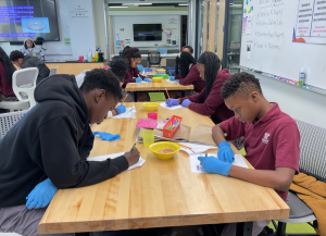 students wearing rubber gloves lean over their desk working on an experiment